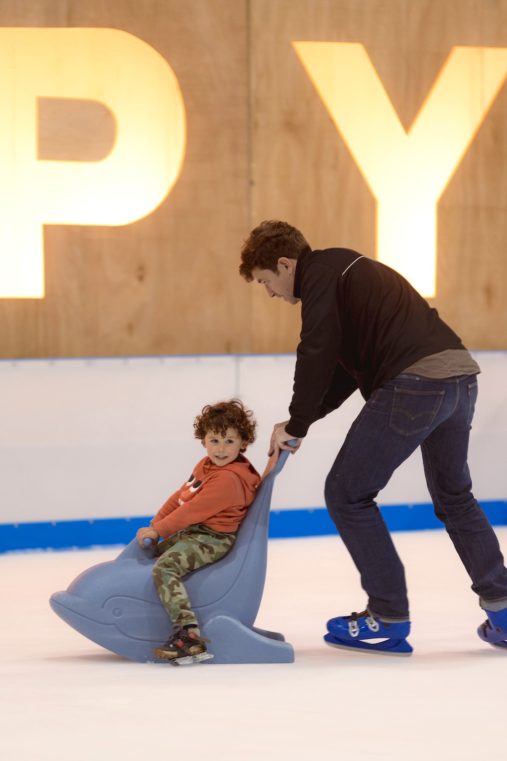 Man ice skating and pushing young child around on a training seal Propyard Winter Wonderland Ice skating in Bristol
