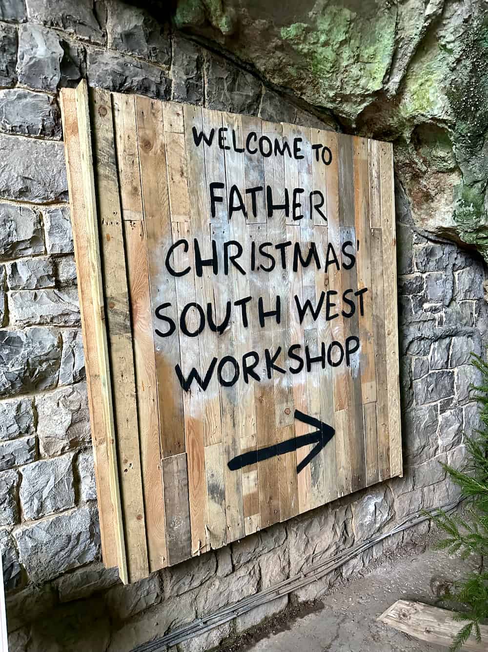 Rustic wooden sign at the entrance to Gough's Cave Santa Grotto reading, "Welcome to Father Christmas South West Workshop"